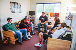 A large group of students hang out in the common area of an apartment on campus.